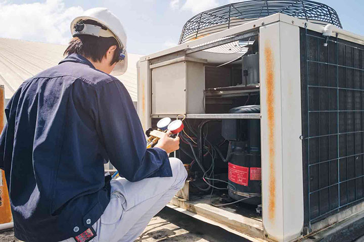Technician checks gauges while servicing an outdoor AC unit on a rooftop.
